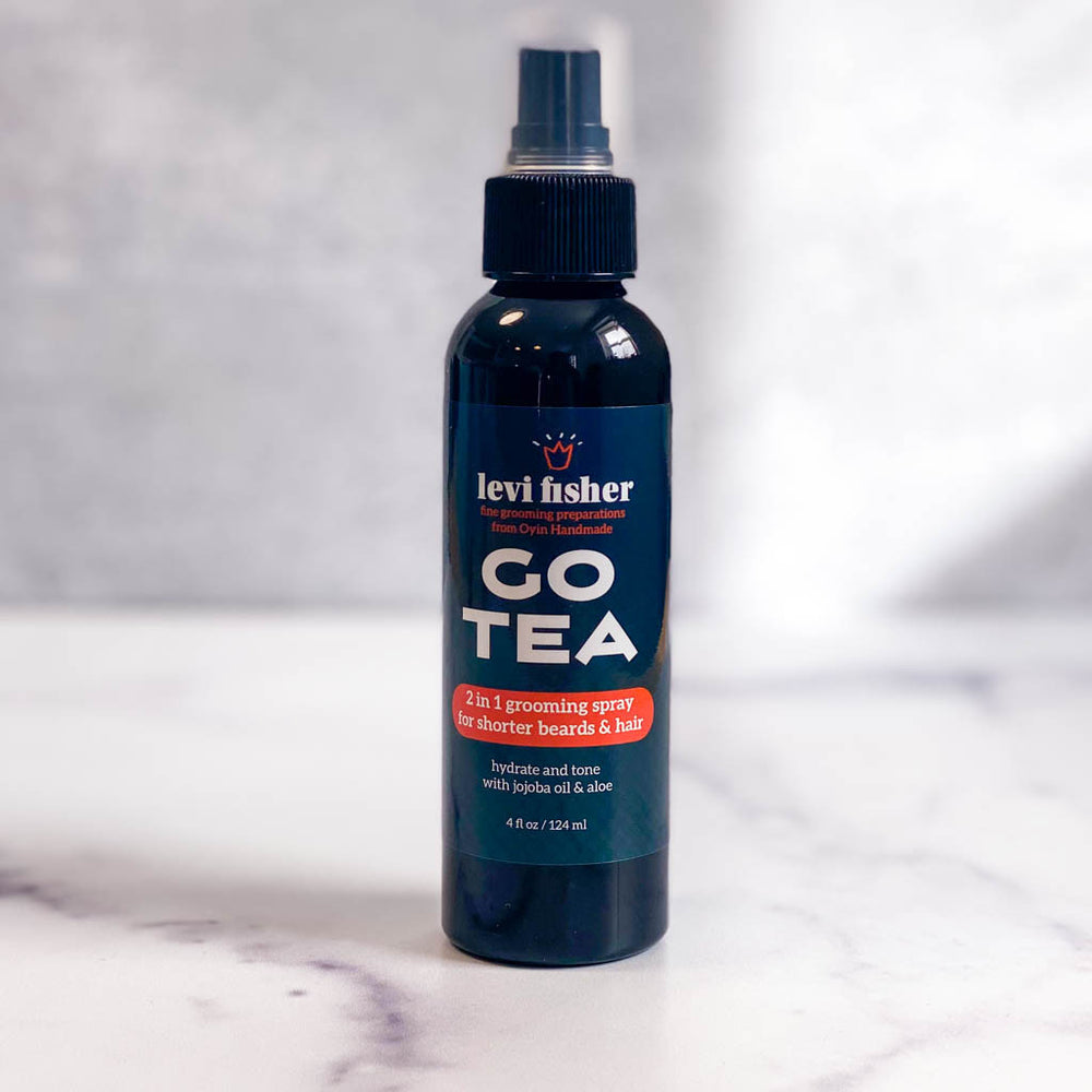 Go tea hydrating beard spray is pictured in a black bottle on marble countertop.